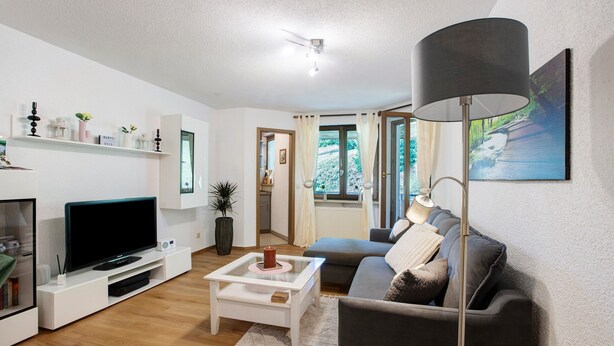 A modern living room with a flat-screen TV, a coffee table, a sofa, a lamp, and a painting on the wall.