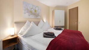 A hotel room with a bed, a nightstand with a lamp, a wardrobe, and a painting on the wall.