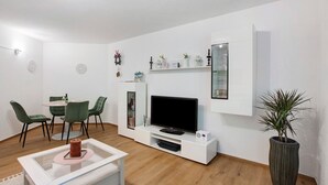A modern living room with a flat-screen TV, green chairs, a white coffee table, and a potted plant.