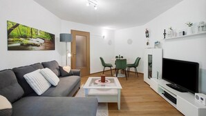 A living room with a sofa, coffee table, TV, and a painting of a forest.