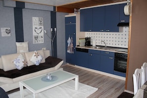 A compact living space with a sofa, coffee table, kitchenette, and a wall with decorative heart-shaped cutouts.