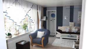 A living room with a blue armchair, a white sofa, a radiator, and a door with a blue flower decoration.