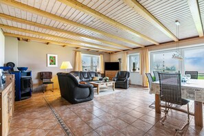 Amplia sala de estar con chimenea, sofás de cuero, una mesa de comedor y ventanas grandes.