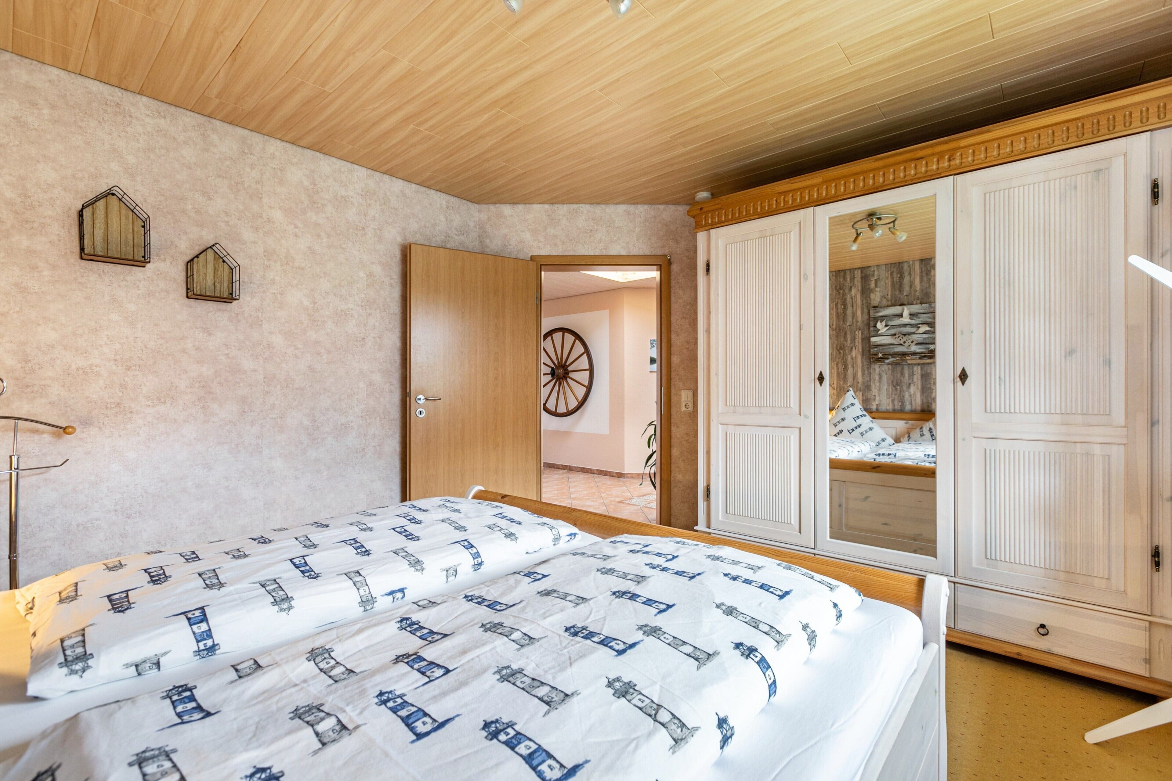 Quarto com cama, guarda-roupa de madeira e porta que dá para outro cômodo.