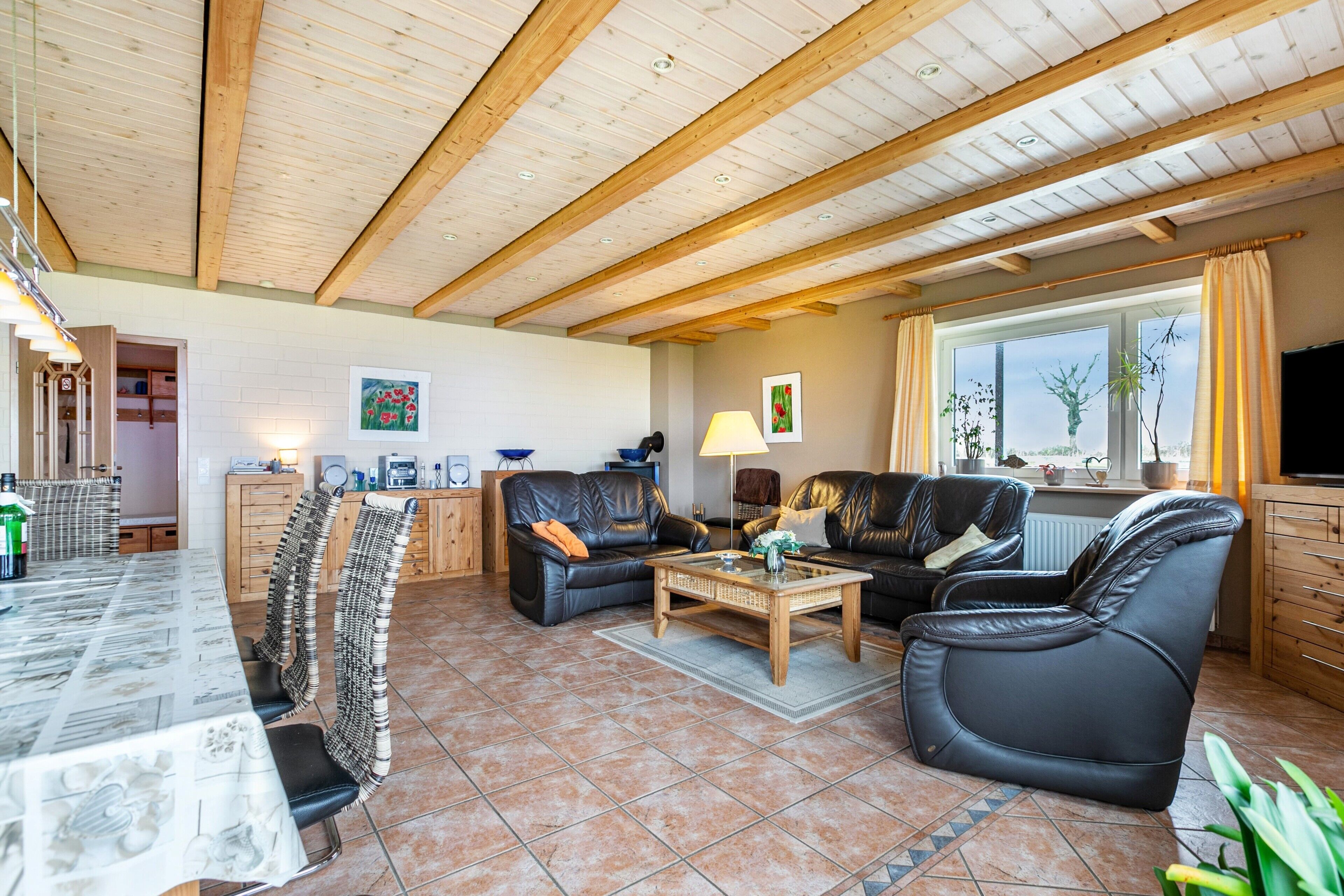 A spacious living room with a high ceiling, a dining area with a long table, and a kitchen area with a window.