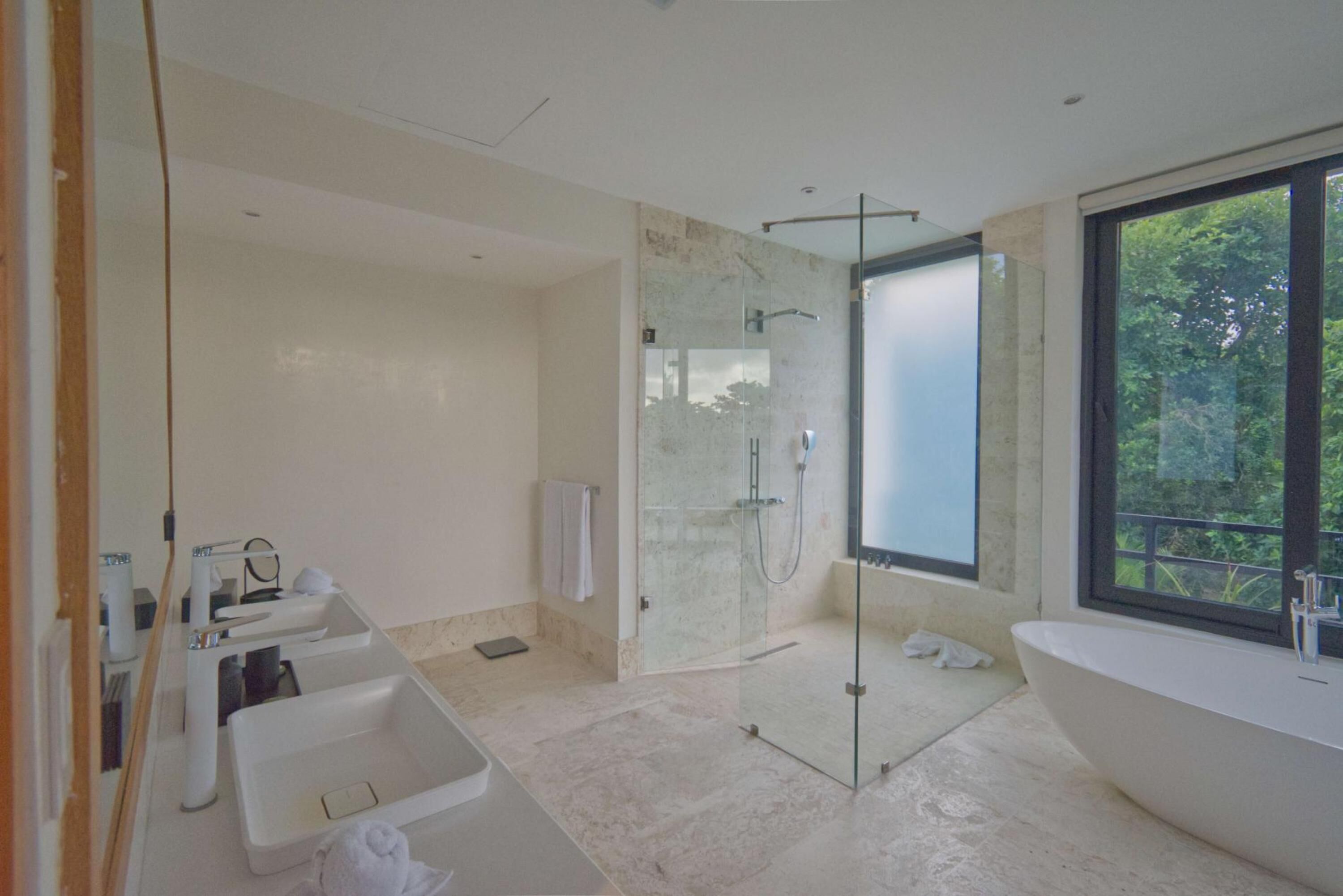Ein modernes Badezimmer mit einer großen Badewanne, einer gläsernen Dusche und einem großen Fenster mit Blick ins Freie.