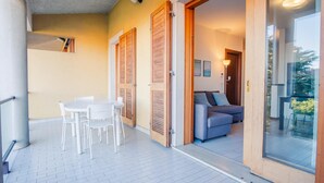 A balcony with a white table and chairs, a grey sofa, and wooden shutters. - Il Roseto - Italian Homing (Desenzano del Garda)