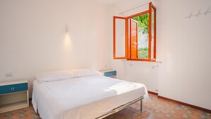 Een slaapkamer met een bed, nachtkastje, ladekast en een raam met een open luik.
