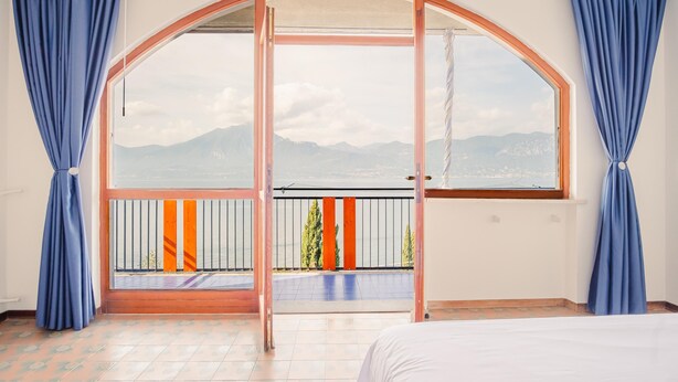 Een kamer met een groot boogvenster, een balkon met oranje leuningen en blauwe gordijnen.