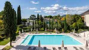 A rectangular swimming pool with lounge chairs and umbrellas, surrounded by greenery and buildings. - Corte Fasanella 25 in Toscolano Maderno (Toscolano Maderno)