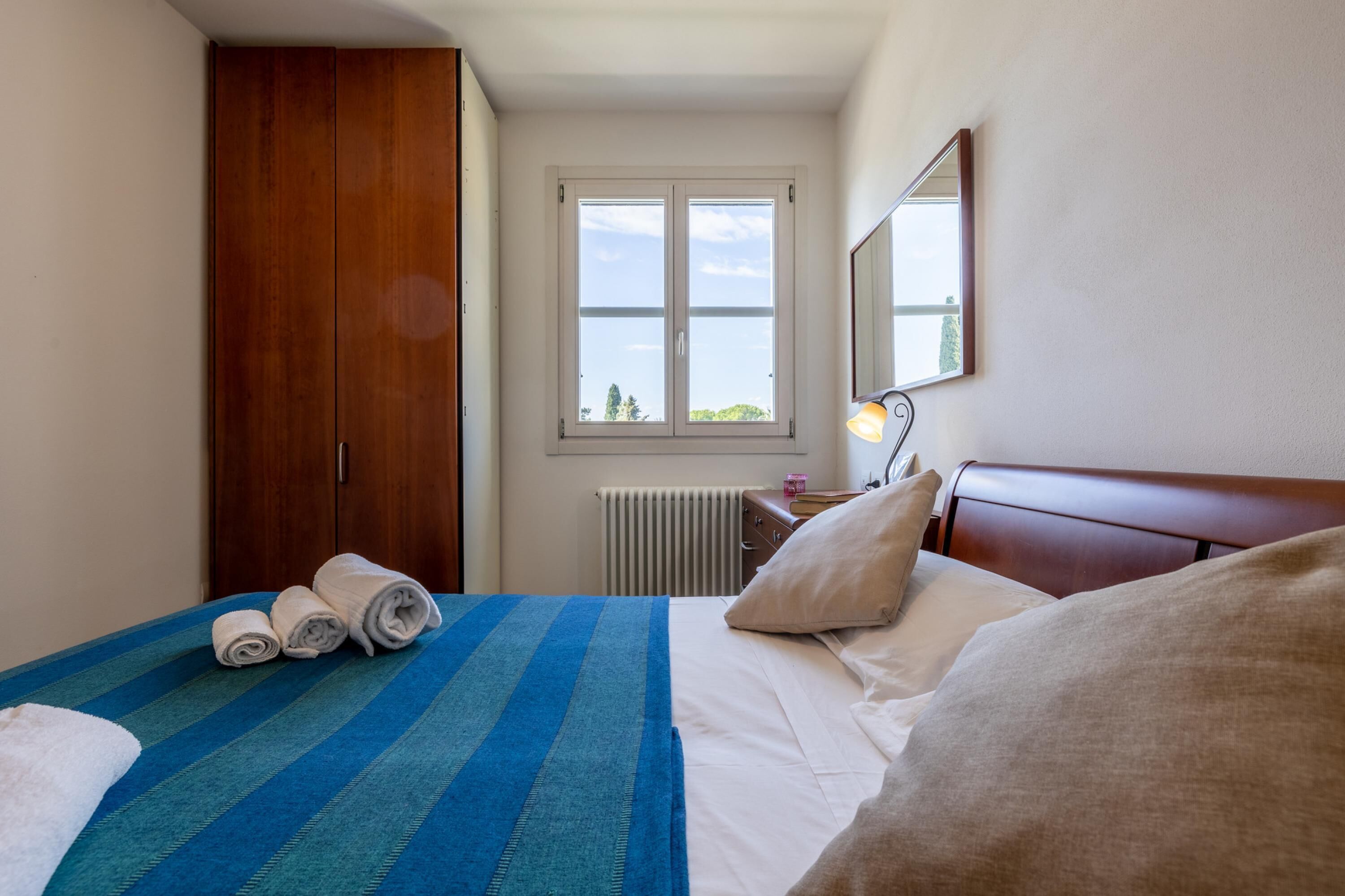 A hotel room with a bed, a window, a radiator, and a wardrobe.