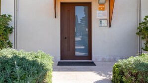 A brown door with a glass panel, a sign reading "SCALA A", and a small outdoor area with a bench and plants. - Corte Fasanella 25 in Toscolano Maderno (Toscolano Maderno)
