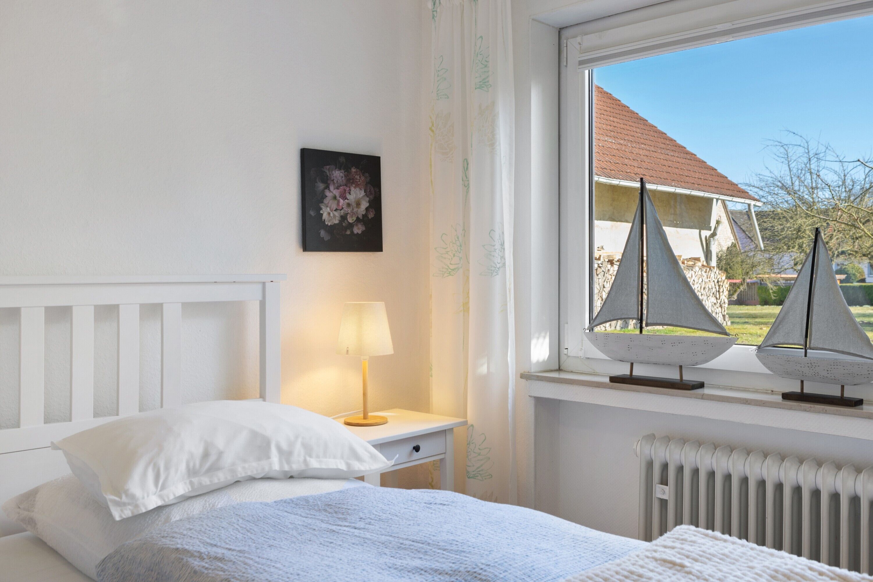 Ein Schlafzimmer mit Bett, Nachttisch, Lampe und einem Fenster mit Blick auf Segelboote.