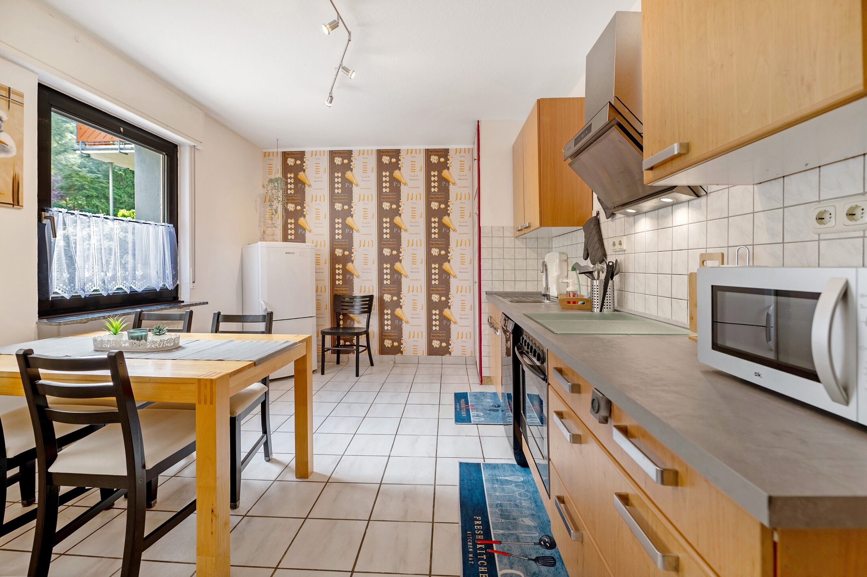 Una cocina con armarios de madera, un microondas y un comedor con sillas y una mesa.
