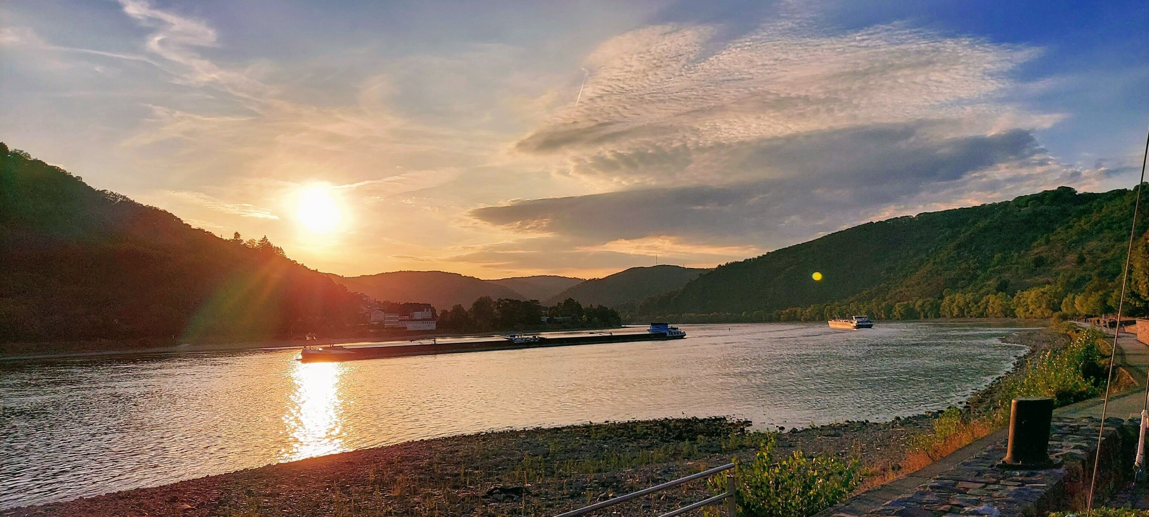 Un río con barcos, un puente y un paisaje montañoso al atardecer.