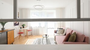 Moderni olohuone, jossa on vaaleanpunainen sohva, pyöreä sohvapöytä ja ruokailutila, jossa on pieni pöytä ja tuolit.