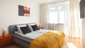 Moderni makuuhuone, jossa on sänky, yöpöydät, seinätaideteos ja ikkuna, jossa on verhot.