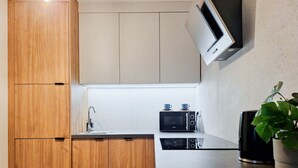 A compact kitchen with wooden cabinets, a microwave, a sink, and a potted plant. - Berka Joselewicza 12/30 (Kraków)