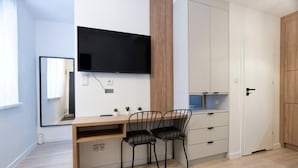A modern, well-lit room with a wooden desk, two black chairs, a flat-screen TV mounted on the wall, and a white wardrobe with a blue interior. - Berka Joselewicza 12/30 (Kraków)