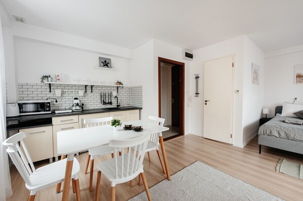 A modern kitchen with white cabinets, a black countertop, and a dining area with a white table and chairs. - Krakowska 5/23b (Kraków)