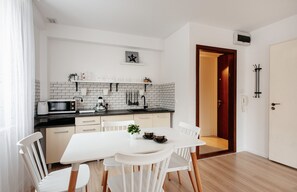 A modern kitchen with white cabinets, a black countertop, and a dining area with white chairs and a table. - Cozy Studio with A/C for 4 guests, Old Town II, Krakowska (Kraków)