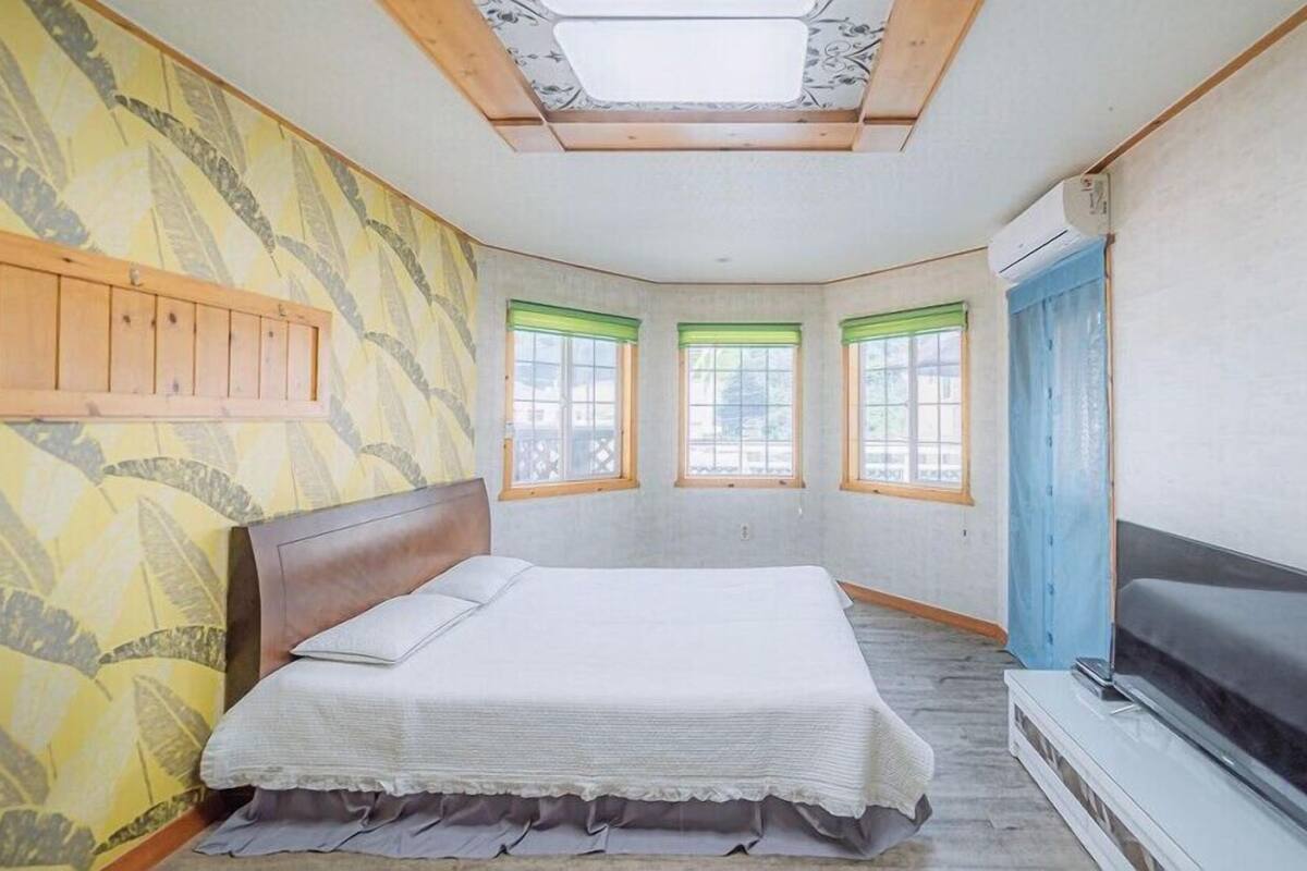 Un dormitorio con una cama, un televisor y tres ventanas con persianas verdes.