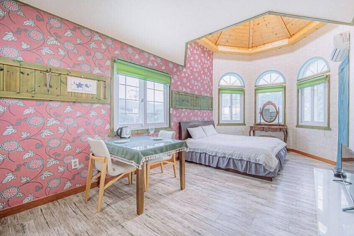 Un dormitorio con techo de madera, una cama, una mesa con sillas y una ventana.
