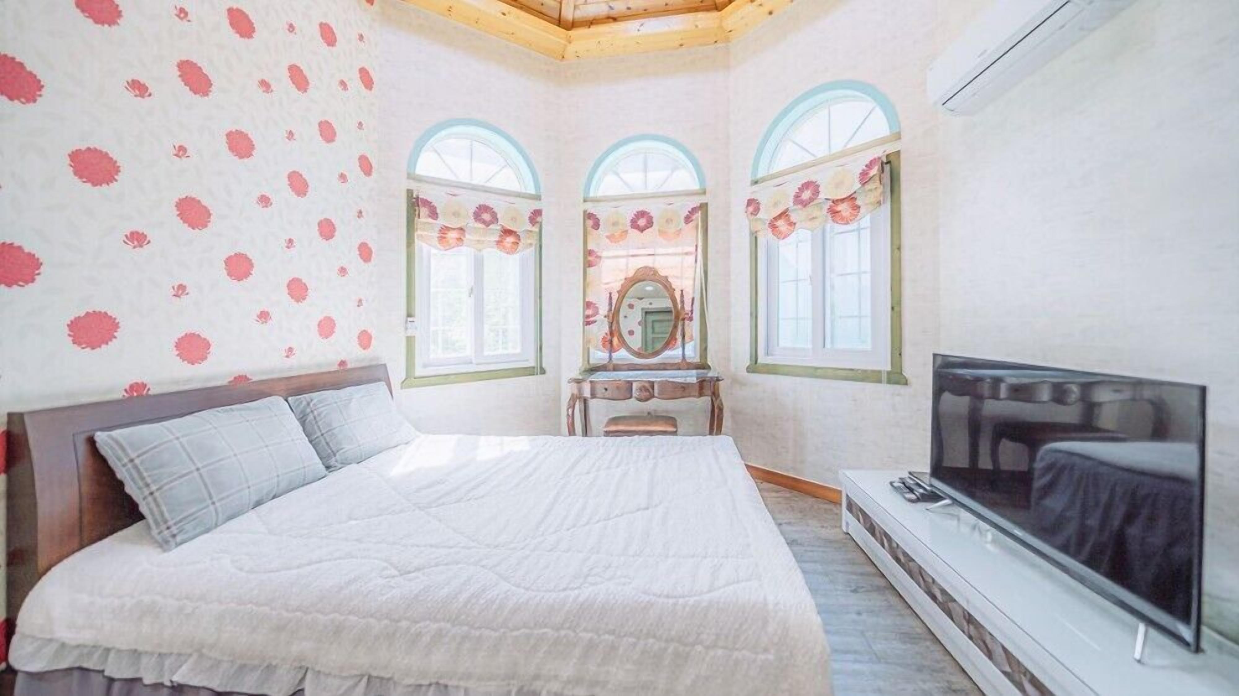 A bedroom with a bed, a vanity with a mirror, and a TV.
