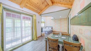 Una habitación con techo de madera, una mesa de comedor con sillas, una cama junto a una ventana y un papel tapiz estampado.