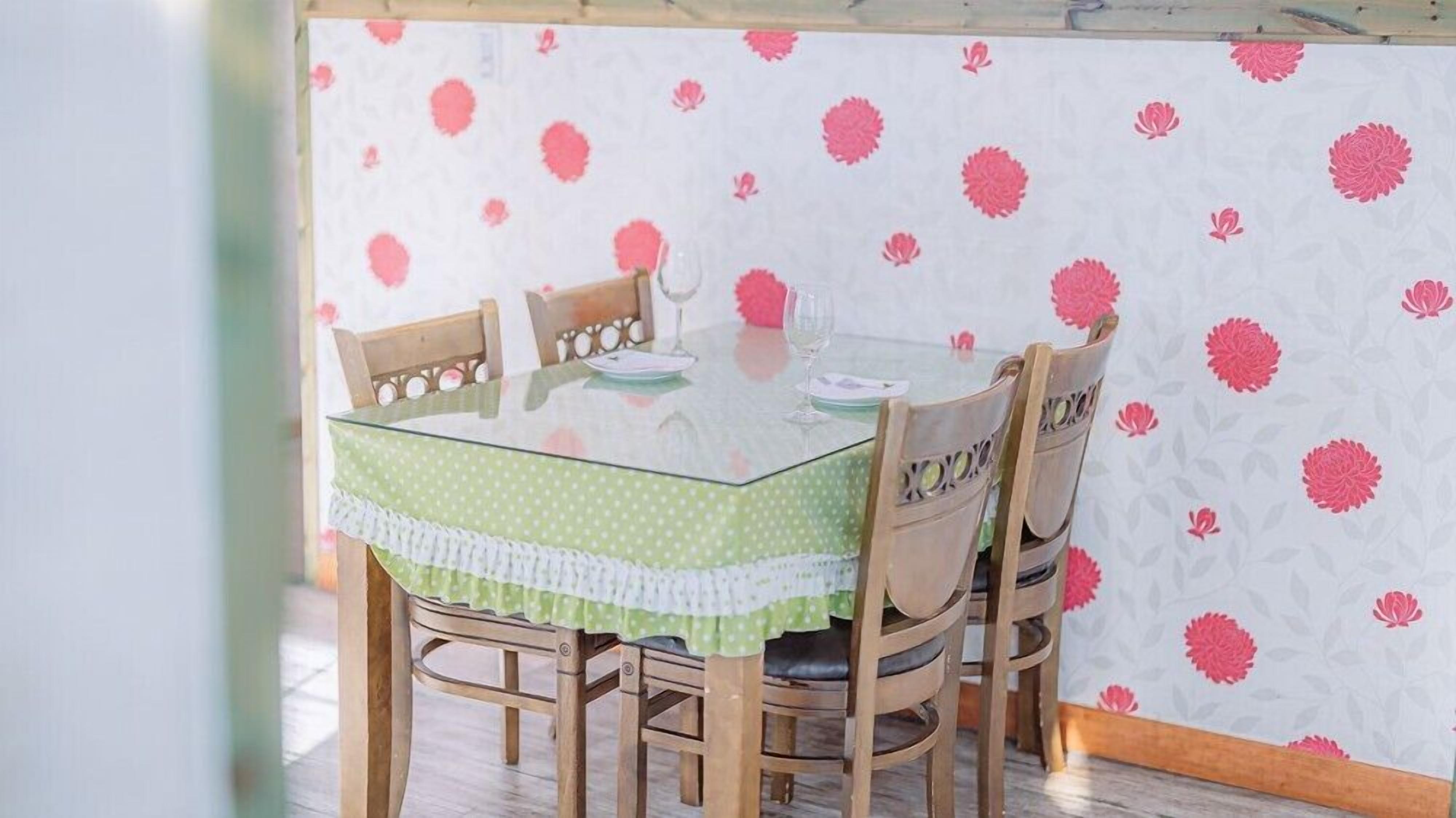 Un comedor con una mesa de vidrio, cuatro sillas de madera y un mantel blanco y verde con lunares.