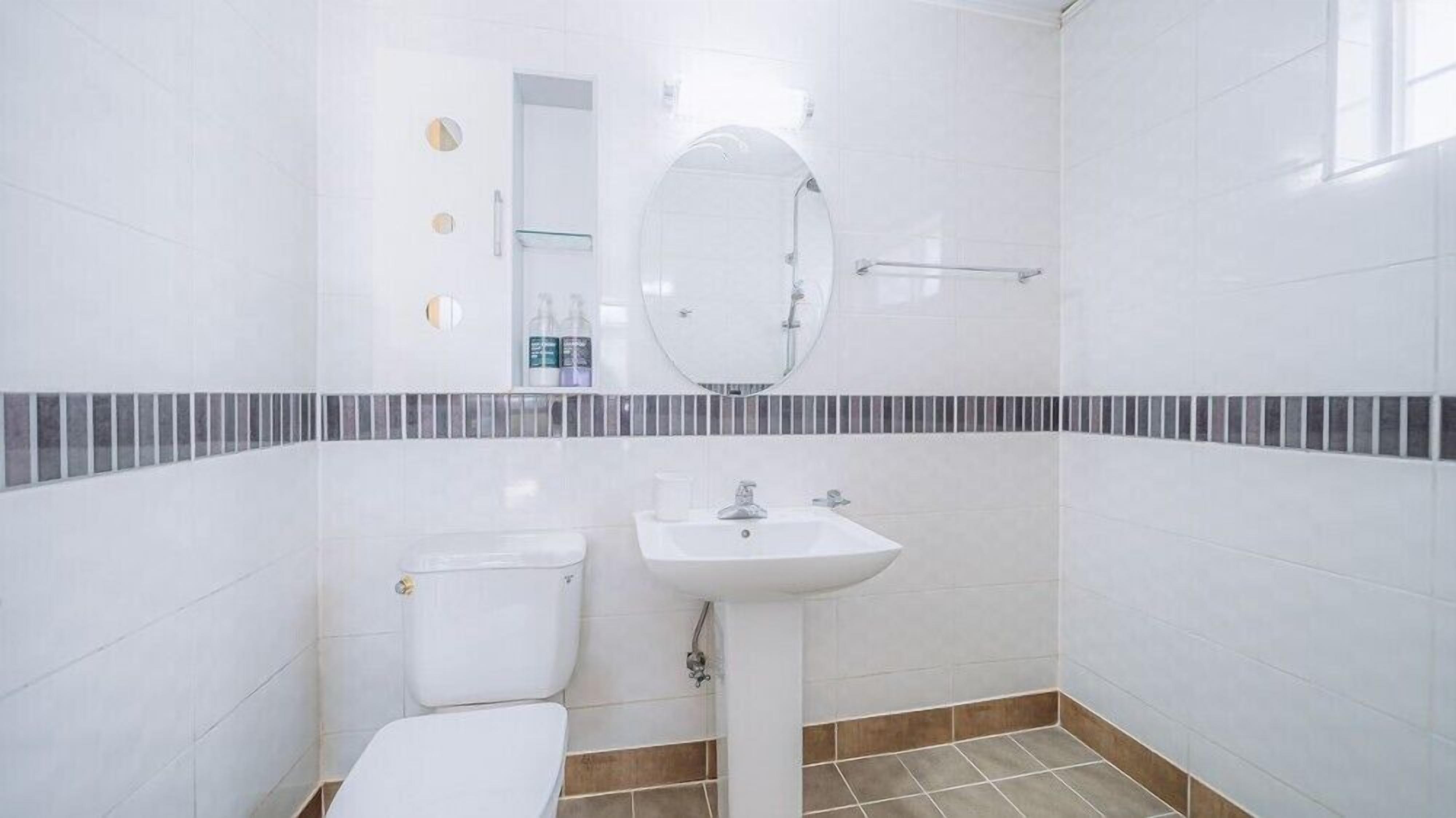 Un baño con azulejos blancos, un lavabo, un inodoro y un espejo.