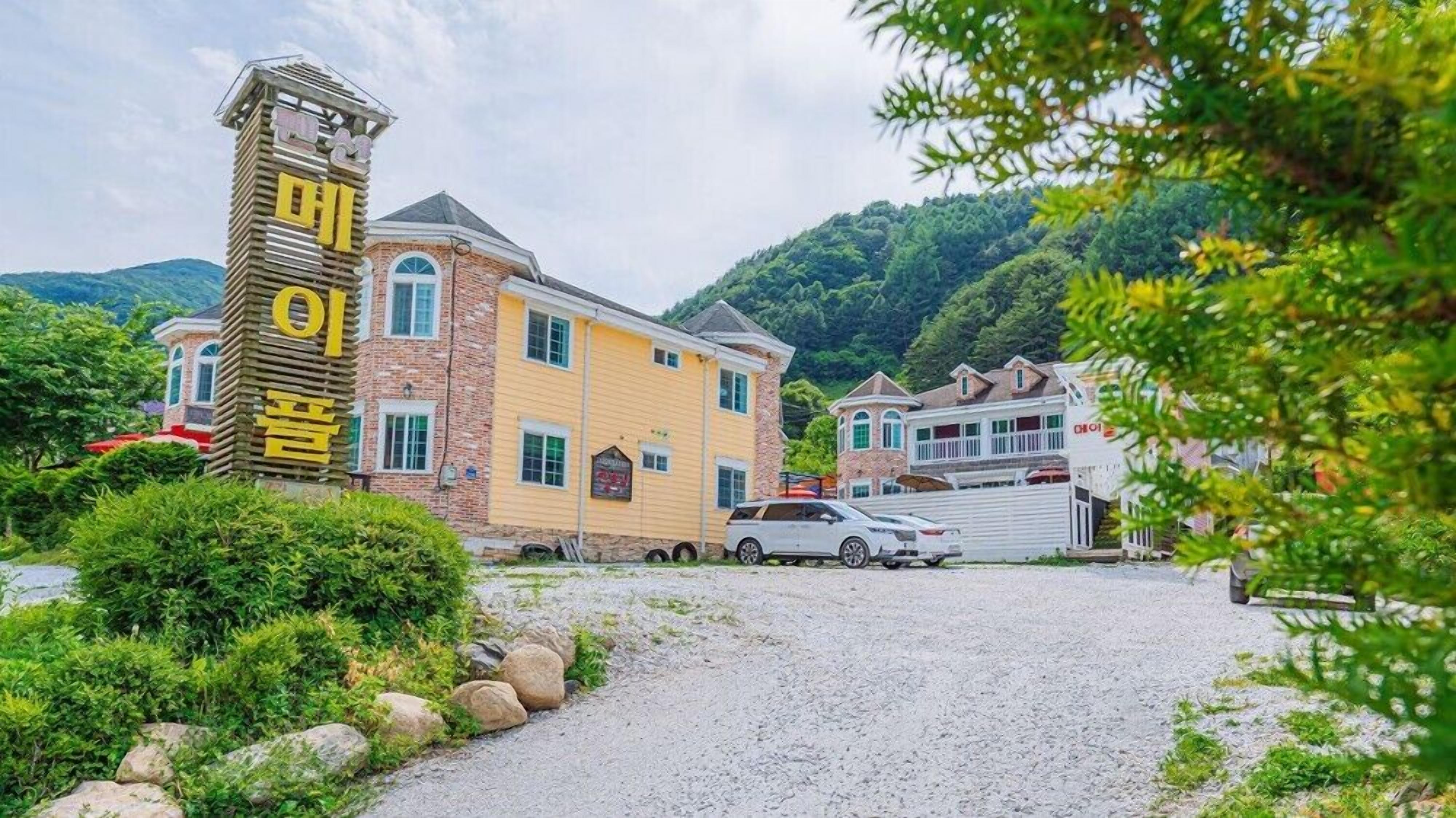 A building with a prominent tower-like structure and a yellow facade, surrounded by greenery and hills.