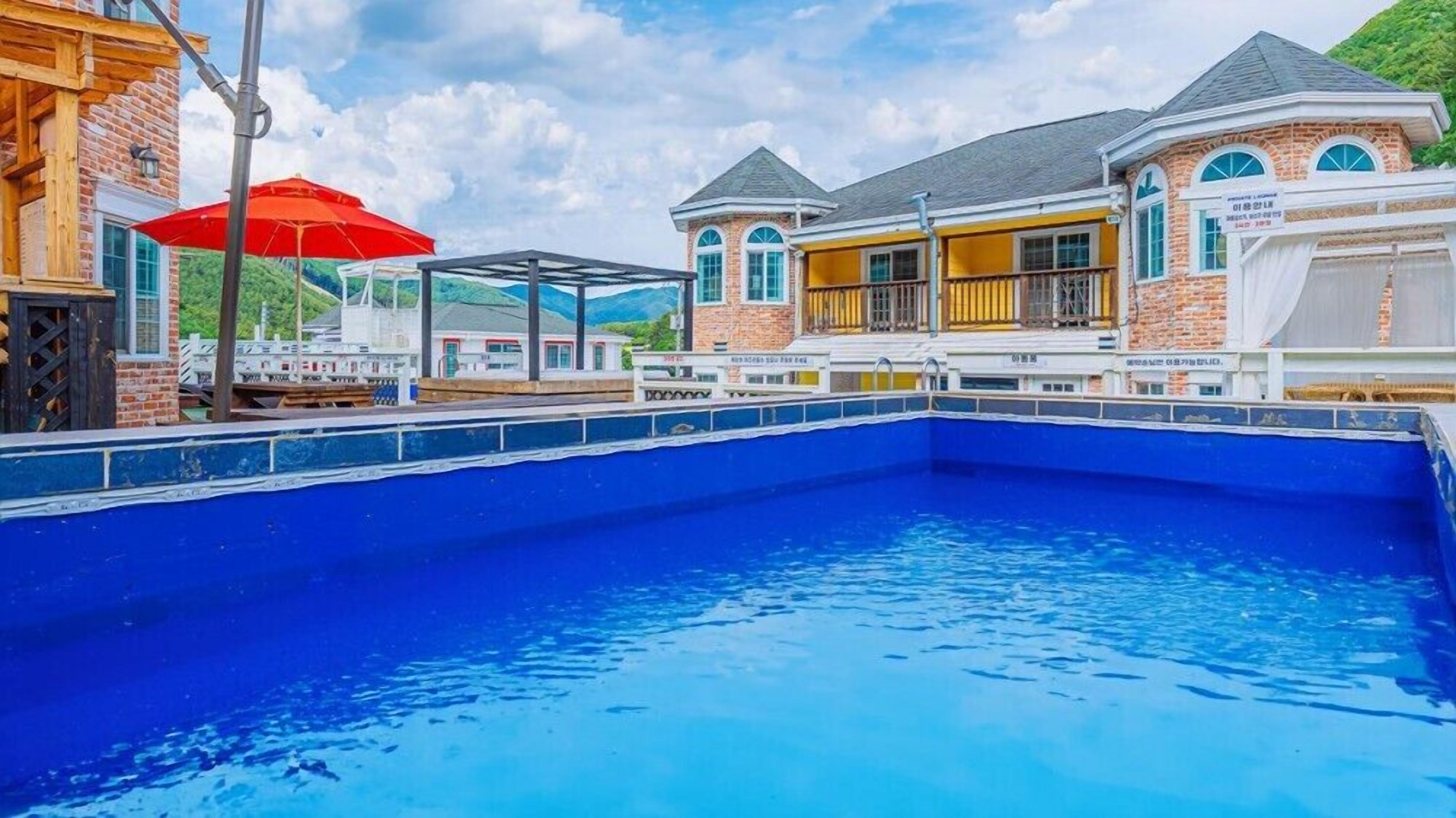 Una piscina con cubierta de madera y un paraguas rojo.