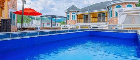 Una piscina con cubierta de madera y un paraguas rojo.