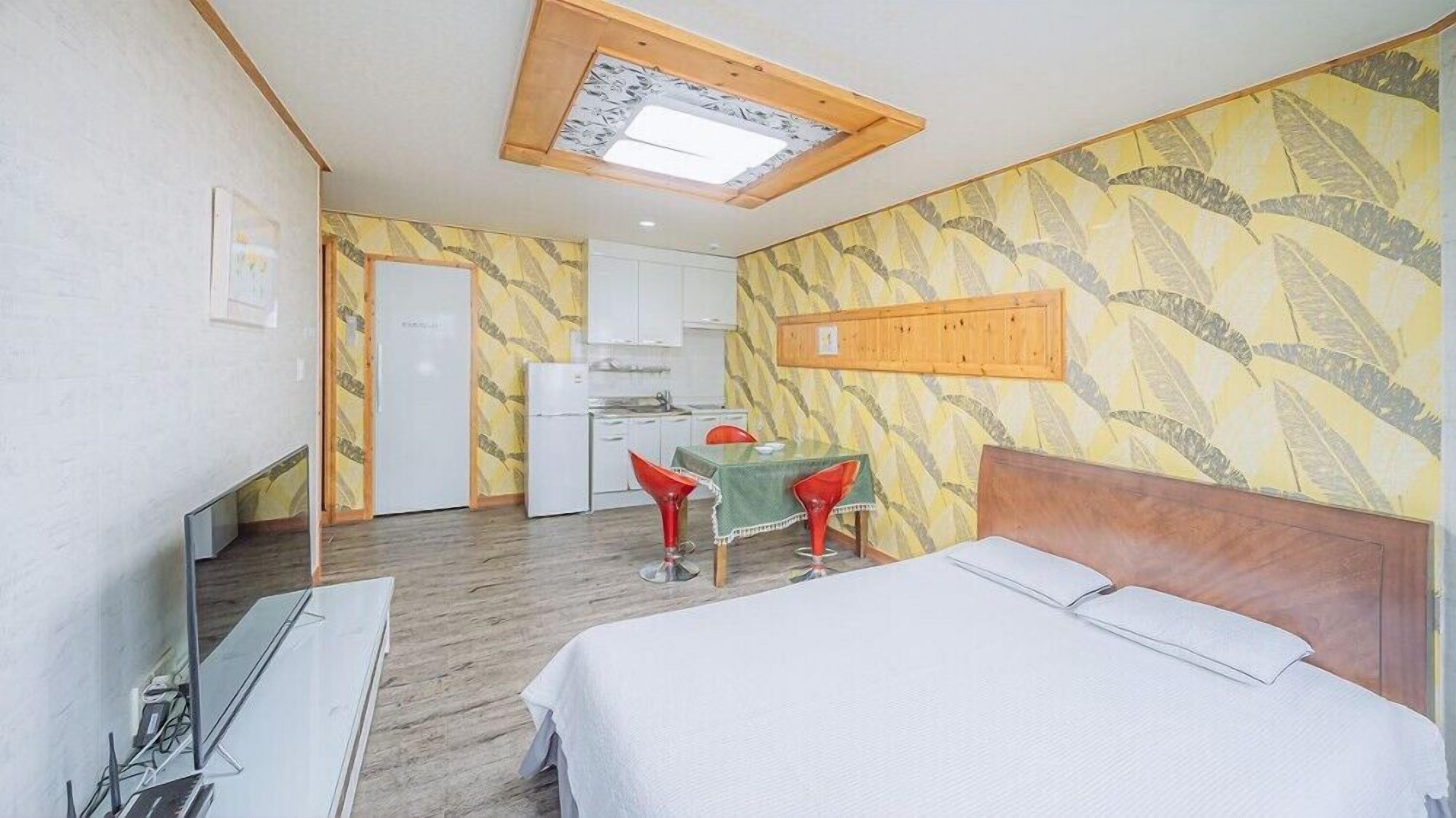 A hotel room with a bed, a small table with chairs, a kitchenette, and a ceiling skylight.