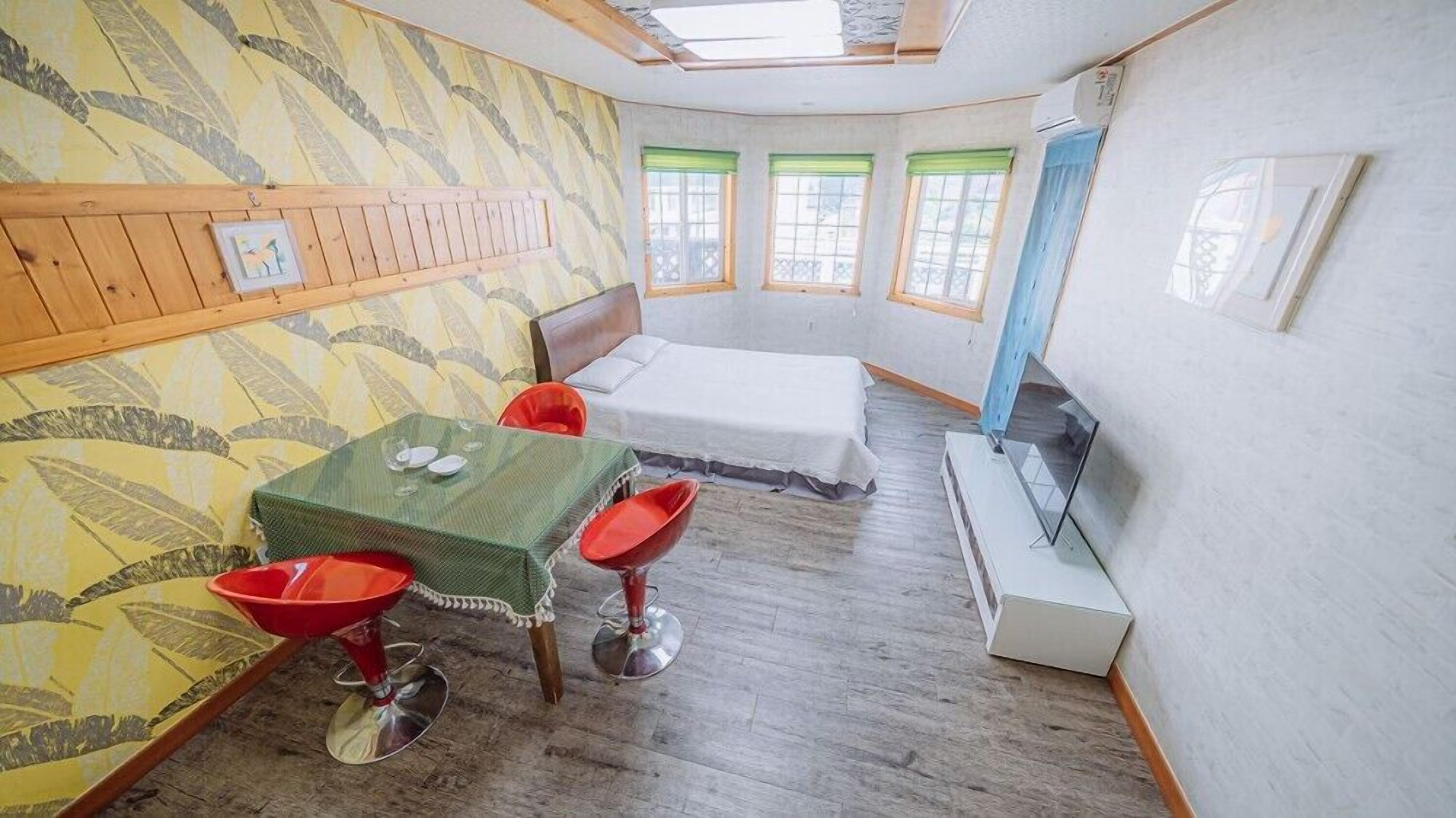 Una stanza compatta con un letto, un tavolino con due sedie, una TV e una finestra con tenda.