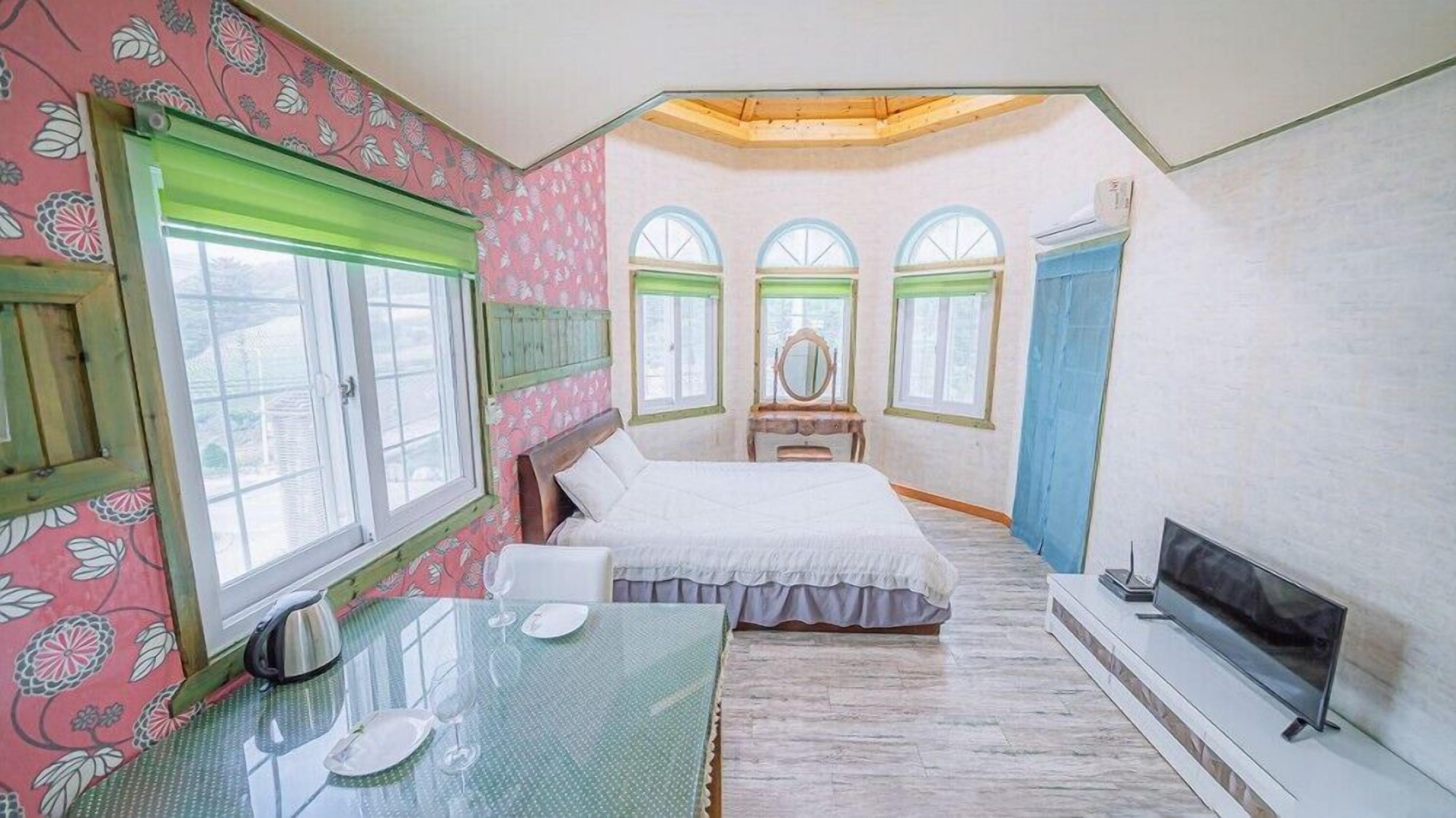 Un dormitorio con cama, tocador con espejo, televisor y una mesa de comedor para cuatro personas.