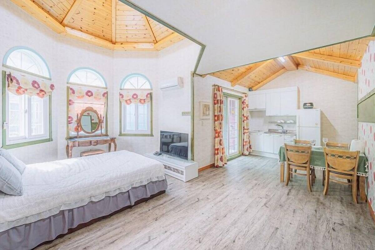 Un dormitorio con cama, tocador con espejo, televisor y una pequeña mesa con sillas.