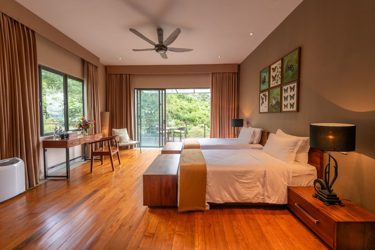 A spacious bedroom with a large bed, a desk, and a view of greenery through the windows.