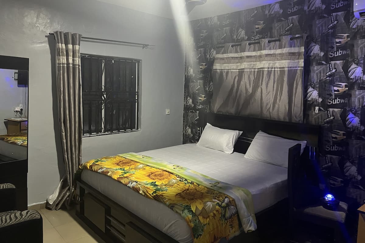 A bedroom with a bed, curtains, a window, a ceiling fan, and a wall with subway-themed wallpaper.