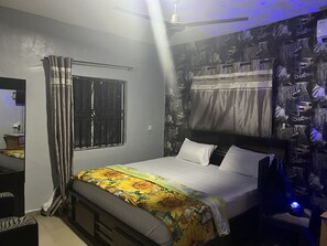 Une chambre à coucher comprenant un lit, des rideaux, une fenêtre, un ventilateur de plafond et un mur recouvert d’un papier peint sur le thème du métro.