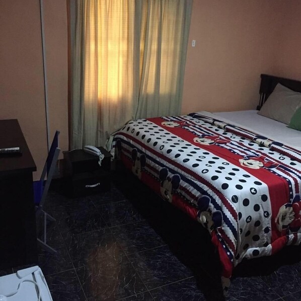 Une chambre à coucher avec un lit recouvert d’une couverture à pois et à rayures, une table de chevet avec une lampe et une fenêtre avec des rideaux.