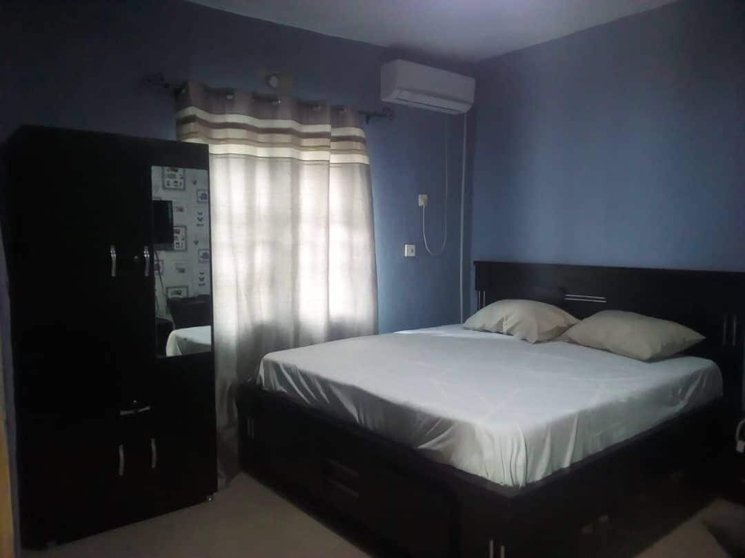 A bedroom with a bed, a wardrobe, a curtain, and an air conditioning unit.