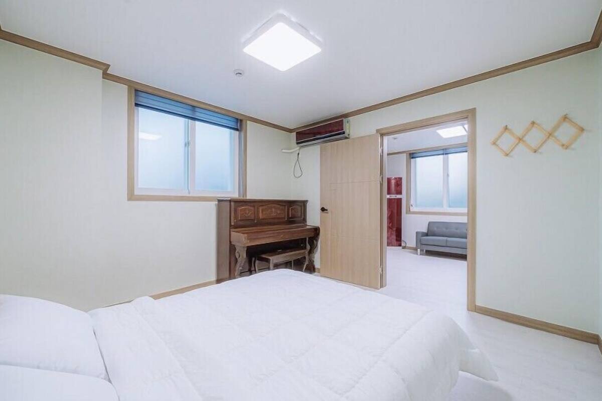 Un dormitorio con una cama, un aparador de madera, una ventana y una puerta que da a otra habitación.