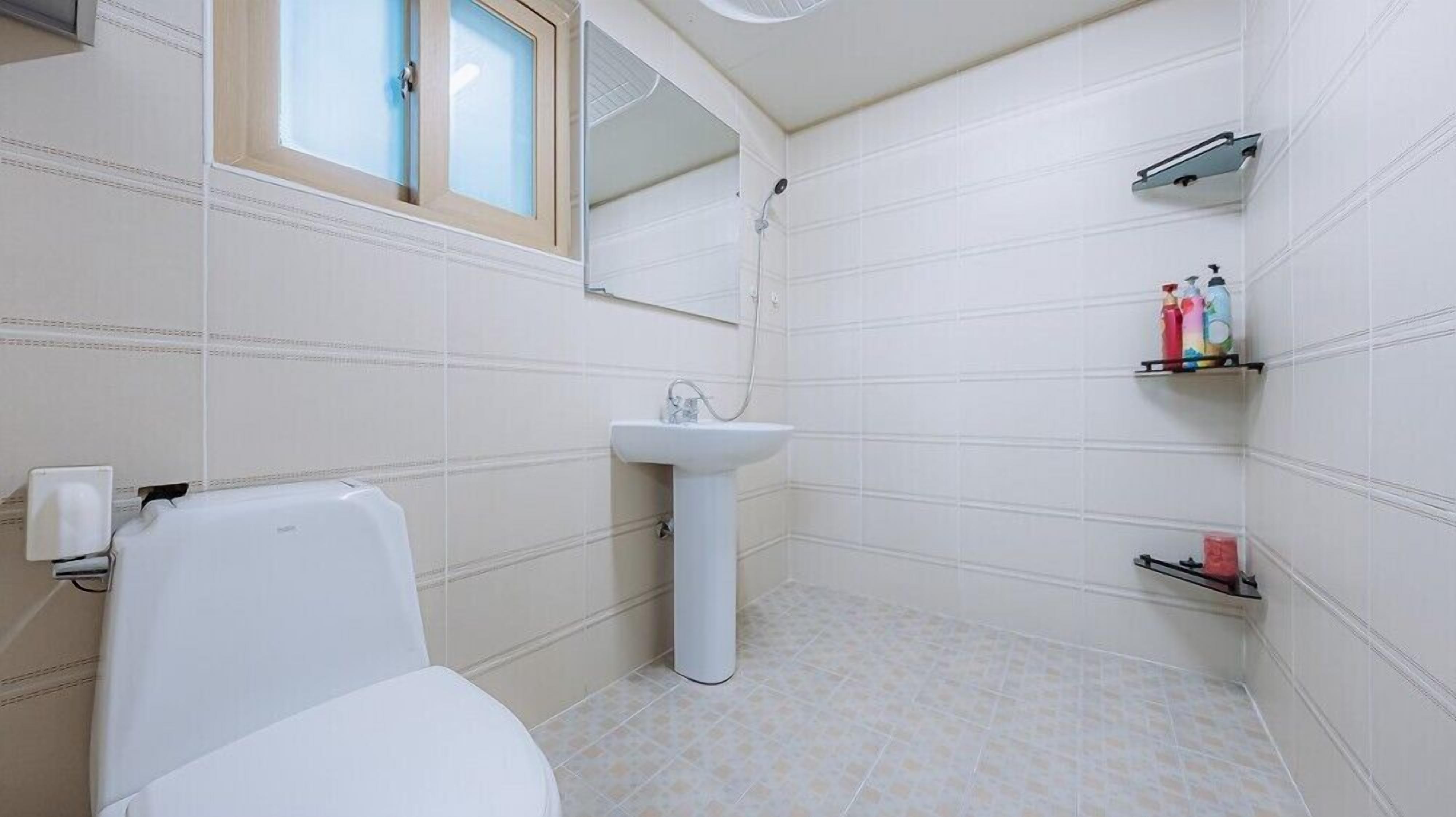 Un baño con inodoro, lavamanos, ducha y estantes con artículos de aseo.