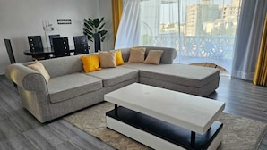A modern living room with a sectional sofa, a white coffee table, and a dining table with chairs.