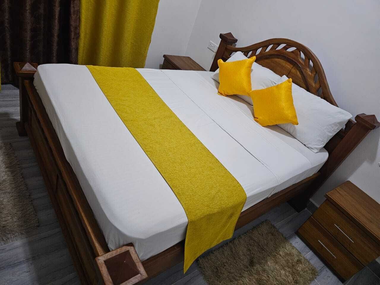 A bed with a wooden frame, white bedding, and a yellow runner.
