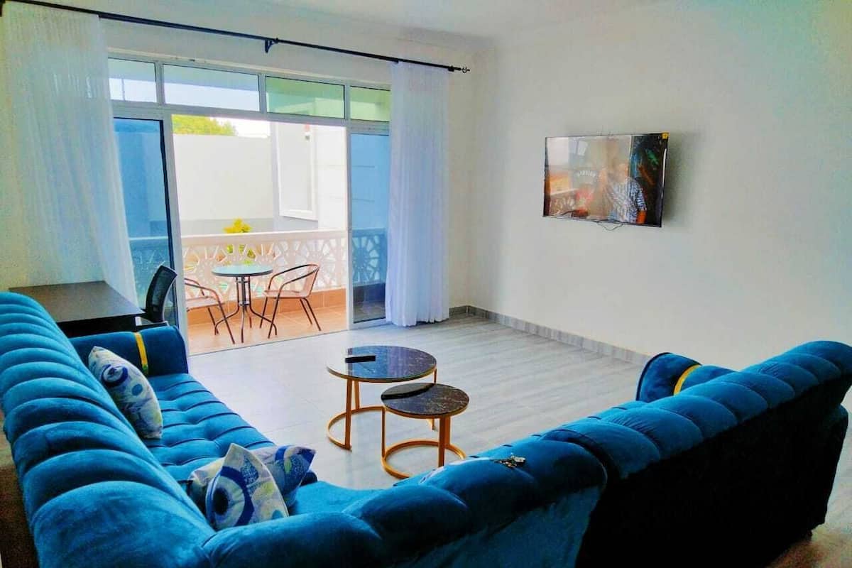 A living room with a blue sofa, two small round tables, and a view of the outside through a glass door.