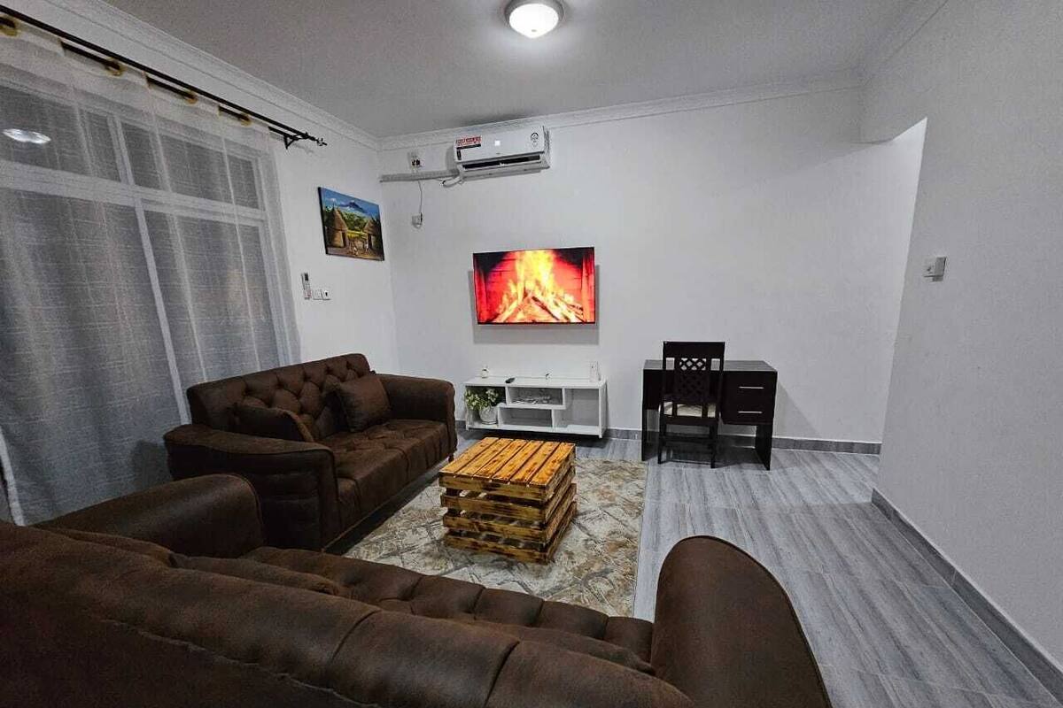 A living room with brown sofas, a wooden coffee table, and a TV displaying a fireplace.