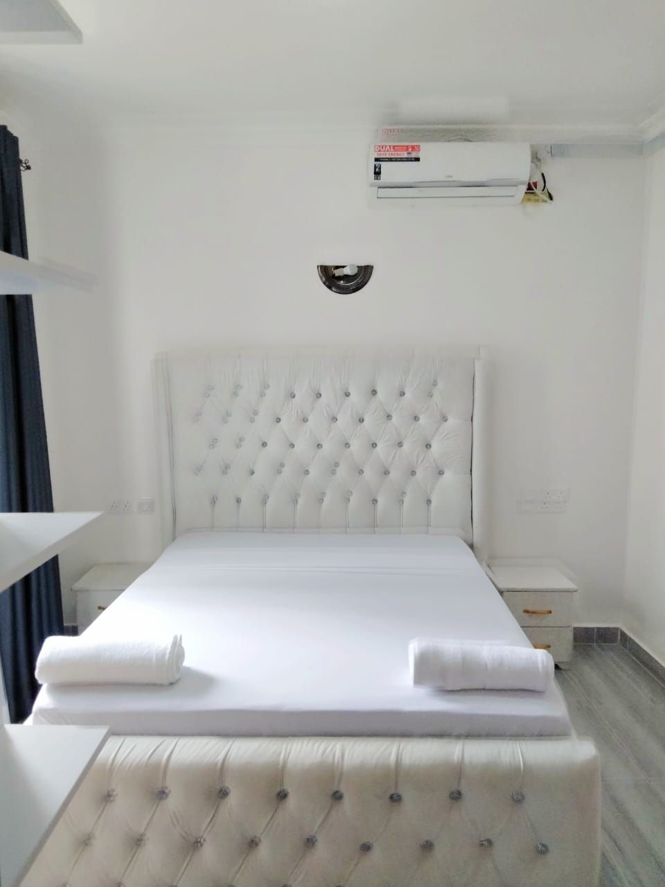 Ein Hotelzimmer mit einem großen Bett, einem Nachttisch und einer Klimaanlage an der Wand.